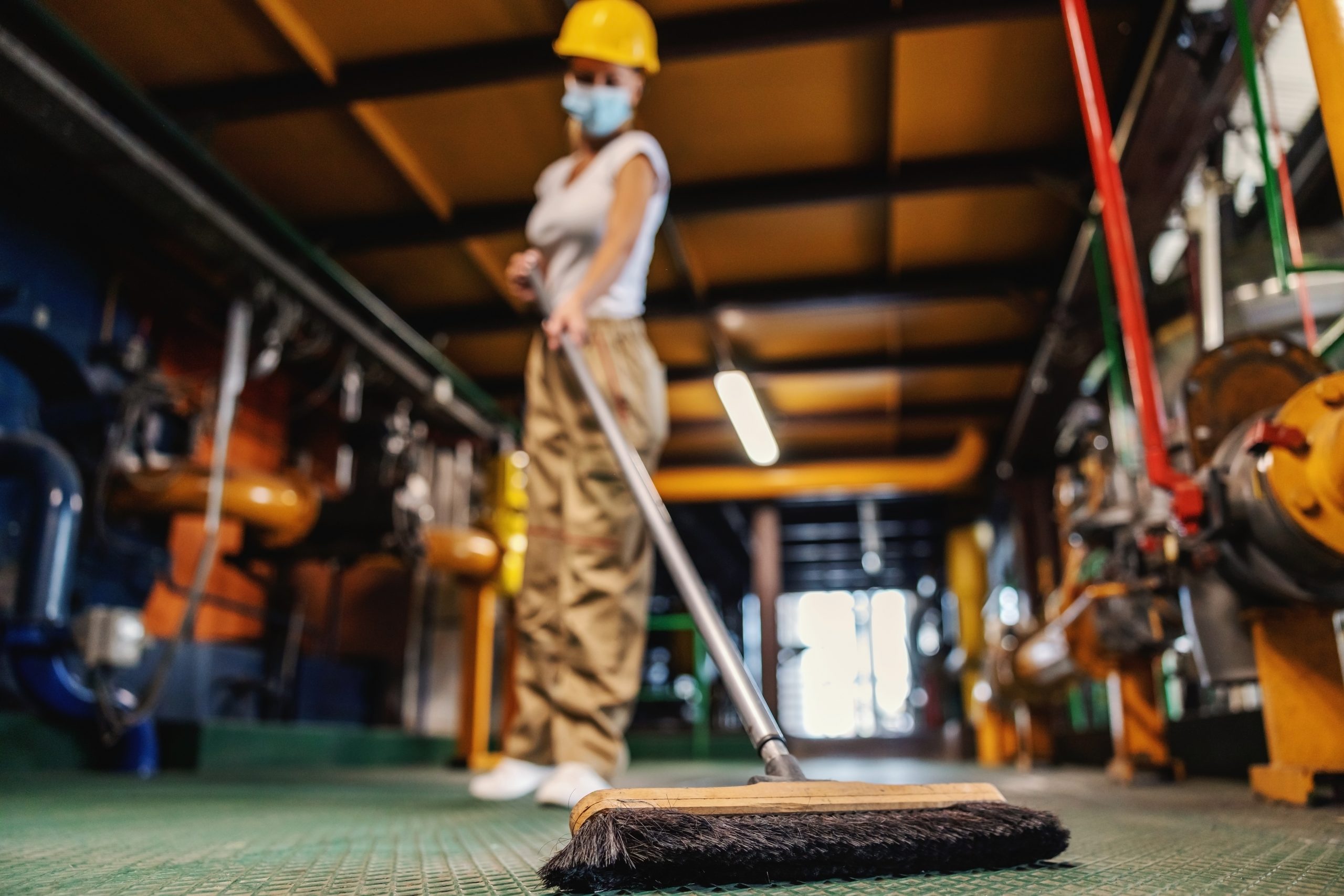 Worker with face mask brooms heating plant facility during corona outbreak.